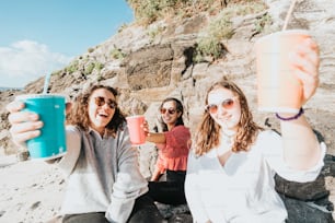 a group of women sitting on a beach holding up drinks