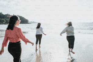 a group of women walking along a beach next to the ocean