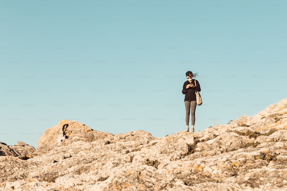uma mulher em pé no topo de uma colina rochosa