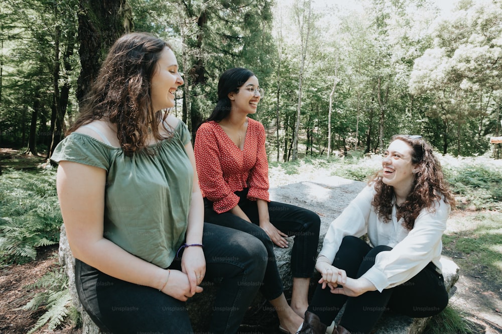 três mulheres sentadas em uma rocha na floresta