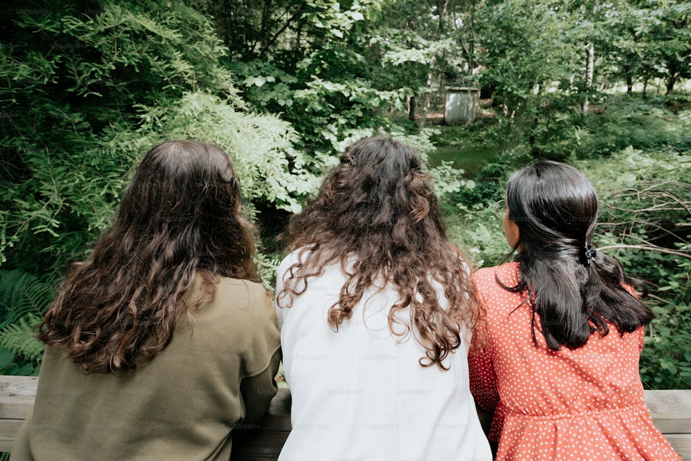 Drei Mädchen, die auf einer Bank sitzen und auf den Wald schauen