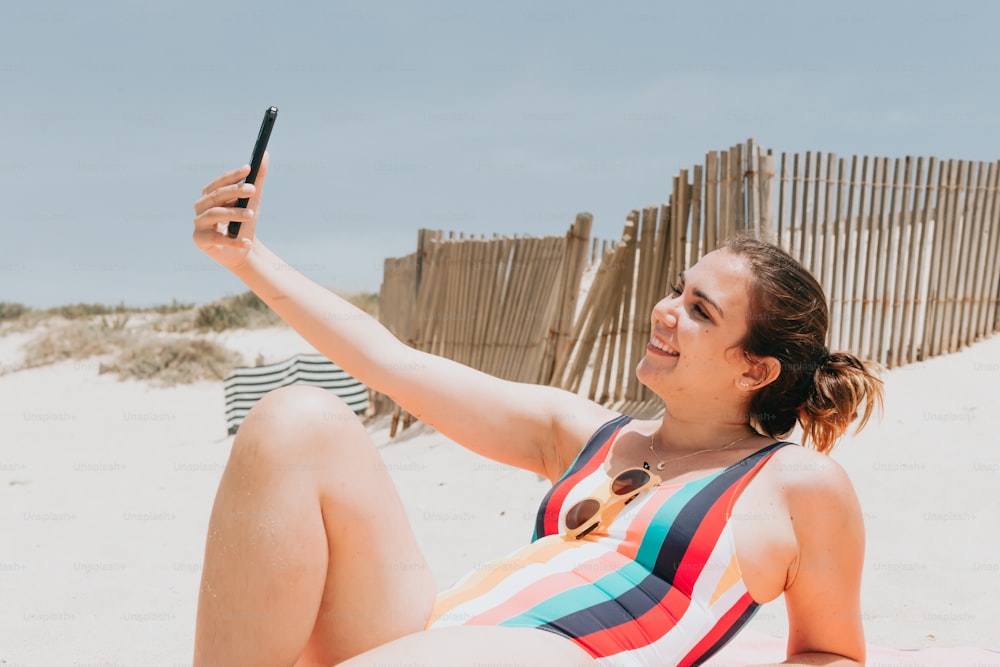 a woman laying on the beach taking a picture with her cell phone