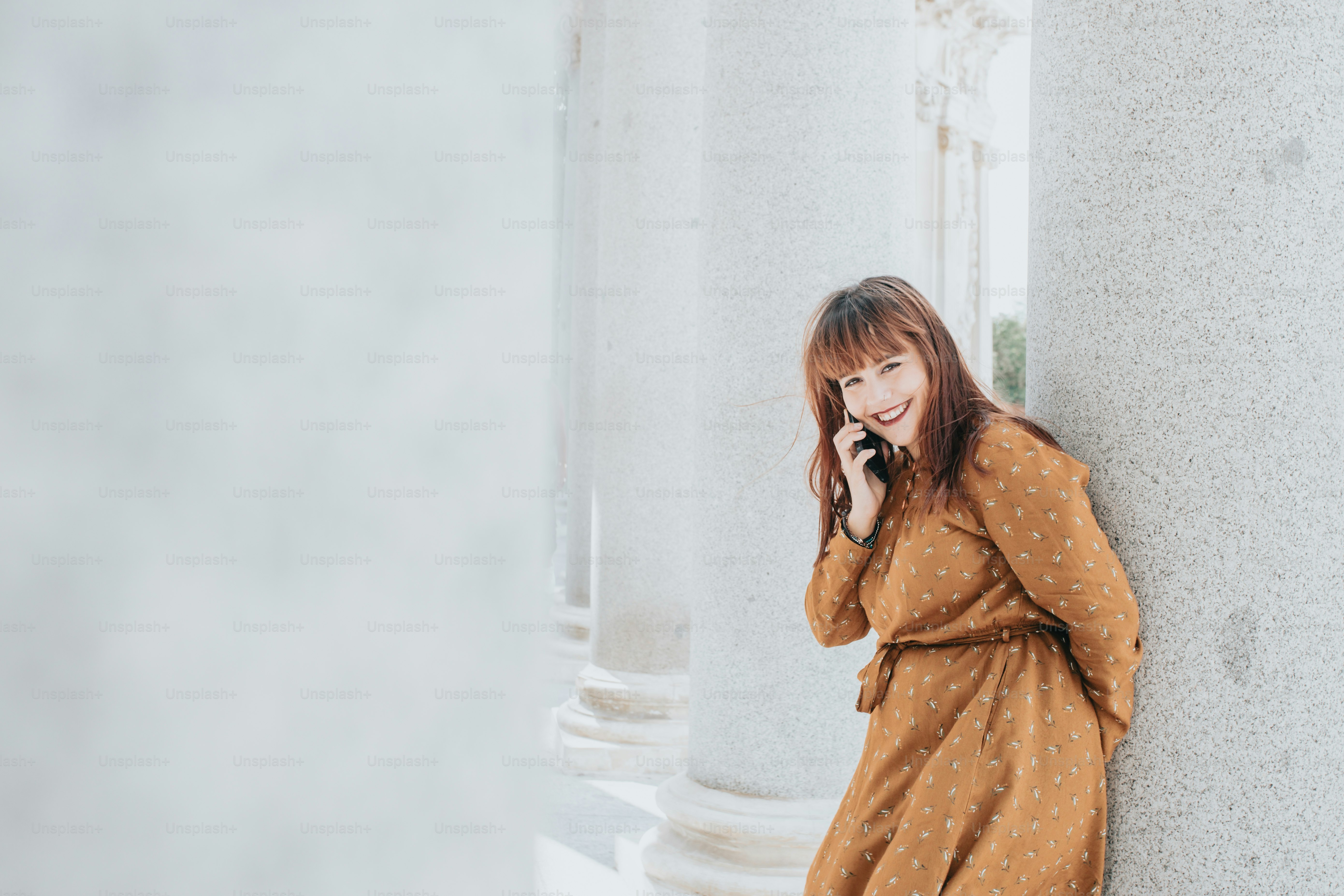 a woman leaning against a column talking on a cell phone