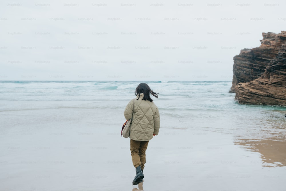 a woman walking along a beach next to the ocean