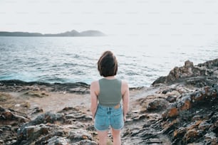 a woman standing on a rocky beach next to the ocean