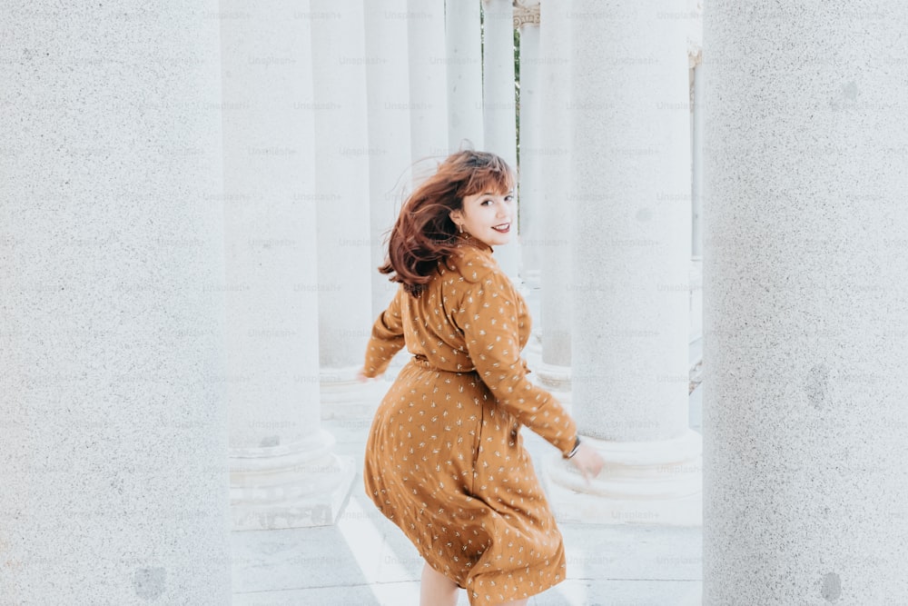 a woman in a brown polka dot dress walking through columns