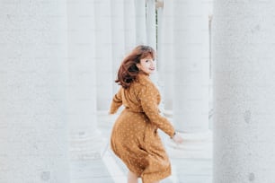 Una mujer con un vestido marrón de lunares caminando a través de columnas