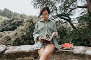 a woman sitting on a wall reading a book