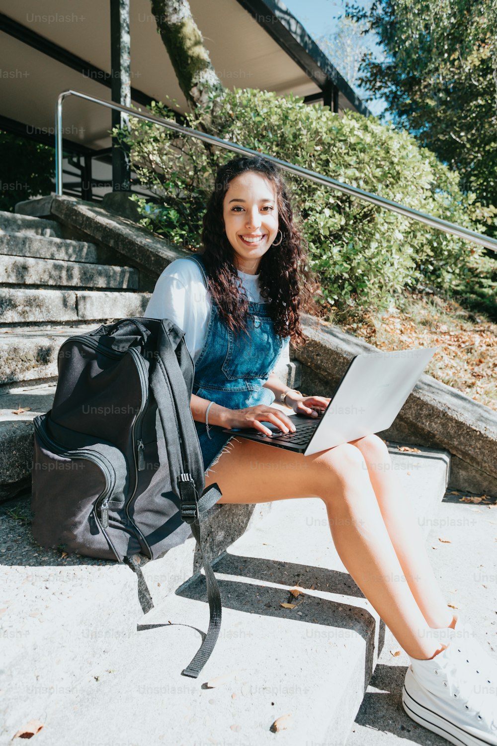 Una donna seduta sui gradini con uno zaino e un computer portatile