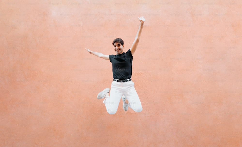 um homem de camisa preta e calça branca pulando no ar