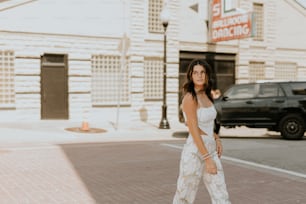 a woman in a white dress is walking down the street