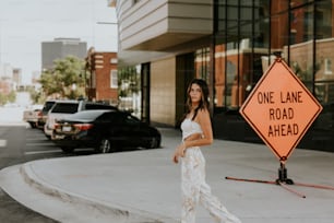 a woman standing on a sidewalk next to a one lane road ahead sign