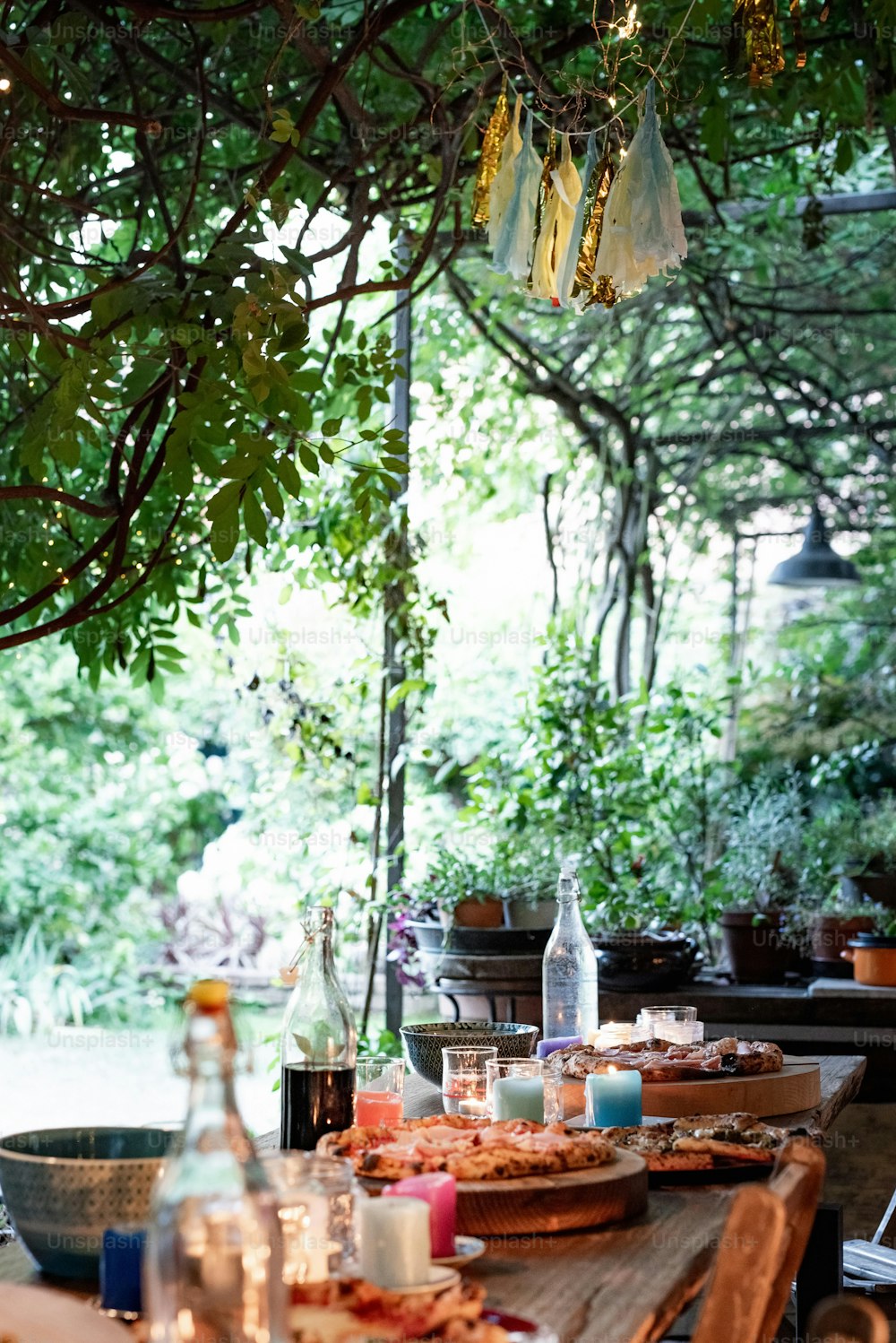 a wooden table topped with plates of food under a tree