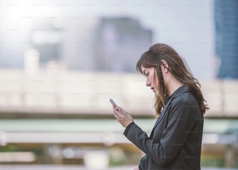 Schöne junge Frau verwendet eine App in ihrem Smartphone-Gerät, um eine Textnachricht vor einem Stadthintergrund zu senden Sie wartet Text von Freund