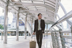 Businessman calling on cell phone while pulling baggage and walking in outdoor covered walkway, panoramic banner with copy space