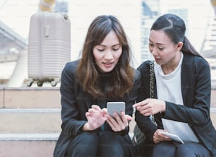 Two businesswomen talking about smart phone in the street with office buildings in the background