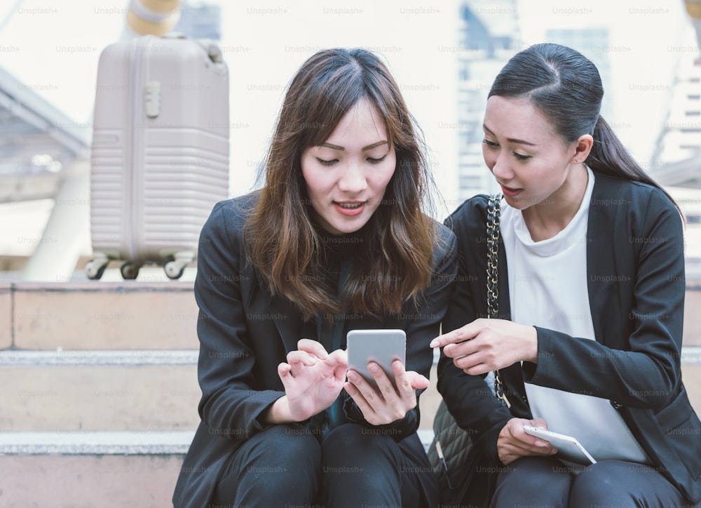 Two businesswomen talking about smart phone in the street with office buildings in the background