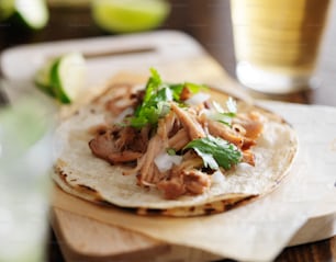 Auténticos tacos mexicanos con carnitas, cilantro y cebolla, y cerveza de fondo