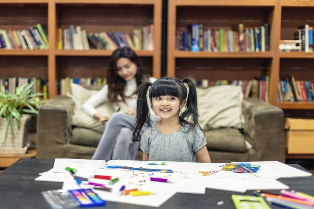 pretty caucasian girl kid enjoy painting crayon color art on paper with mom on sofa background home family concept
