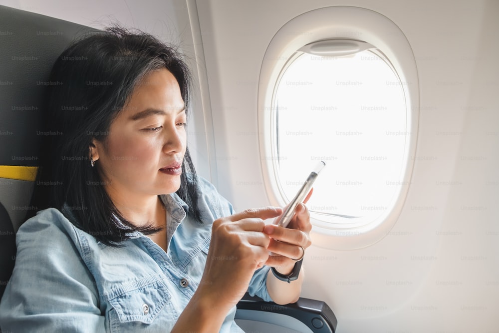 Mulher asiática sentada no assento da janela no avião e ligue o modo avião no telefone celular antes de decolar.