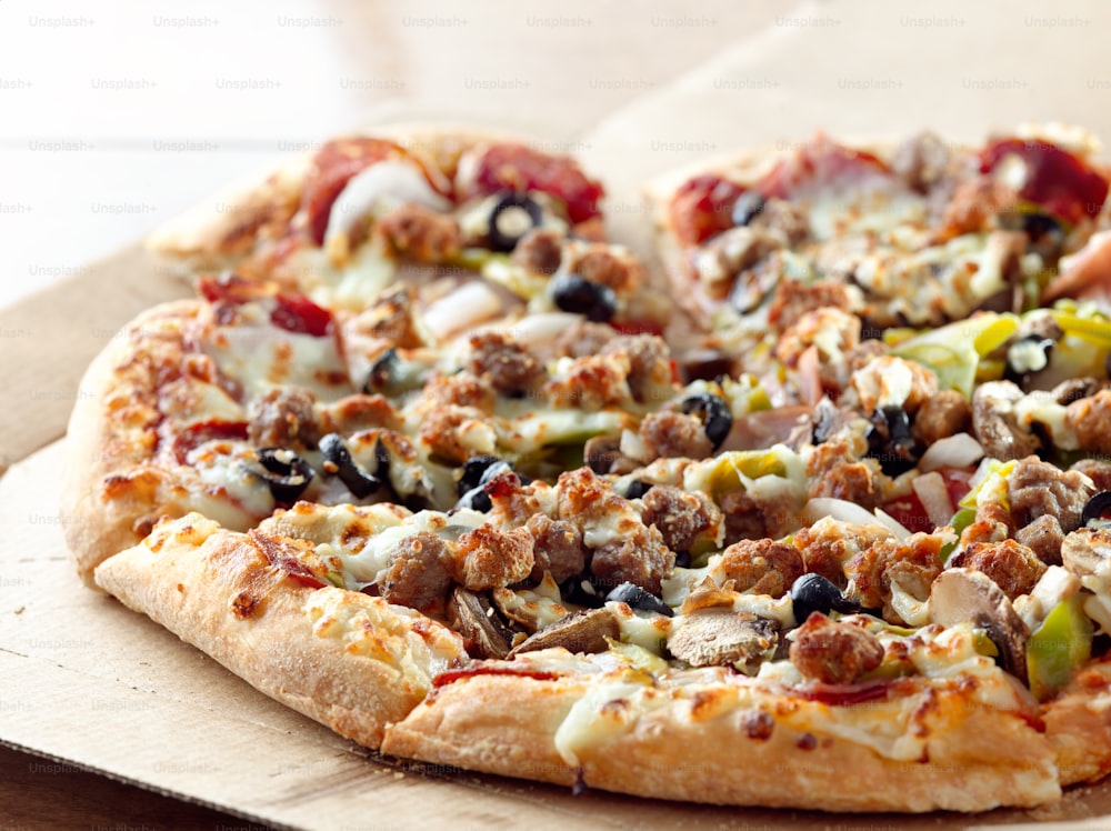Pizza suprême assise sur une boîte en carton avec des saucisses italiennes, des poivrons, des olives noires, des champignons et du pepperoni.