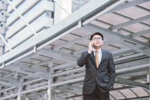 business, technology and people concept - serious businessman with smartphone talking over office building