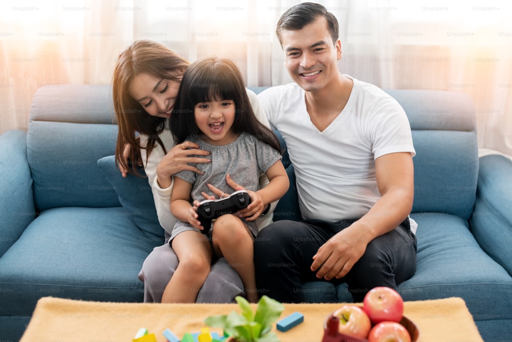 happiness family parent watching daughter play video game and laugh together in living room house concept
