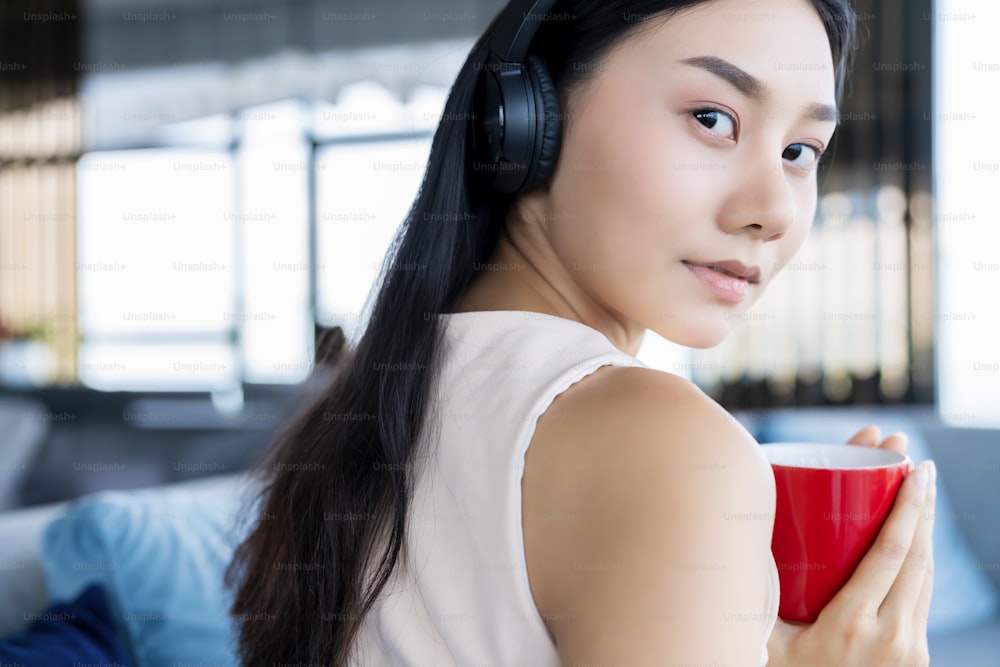 Foto mujer asiática con ropa de trabajo informal tómese un descanso con  café y una revista en el sofá en el fondo de la casa de la sala de estar –  Auriculares