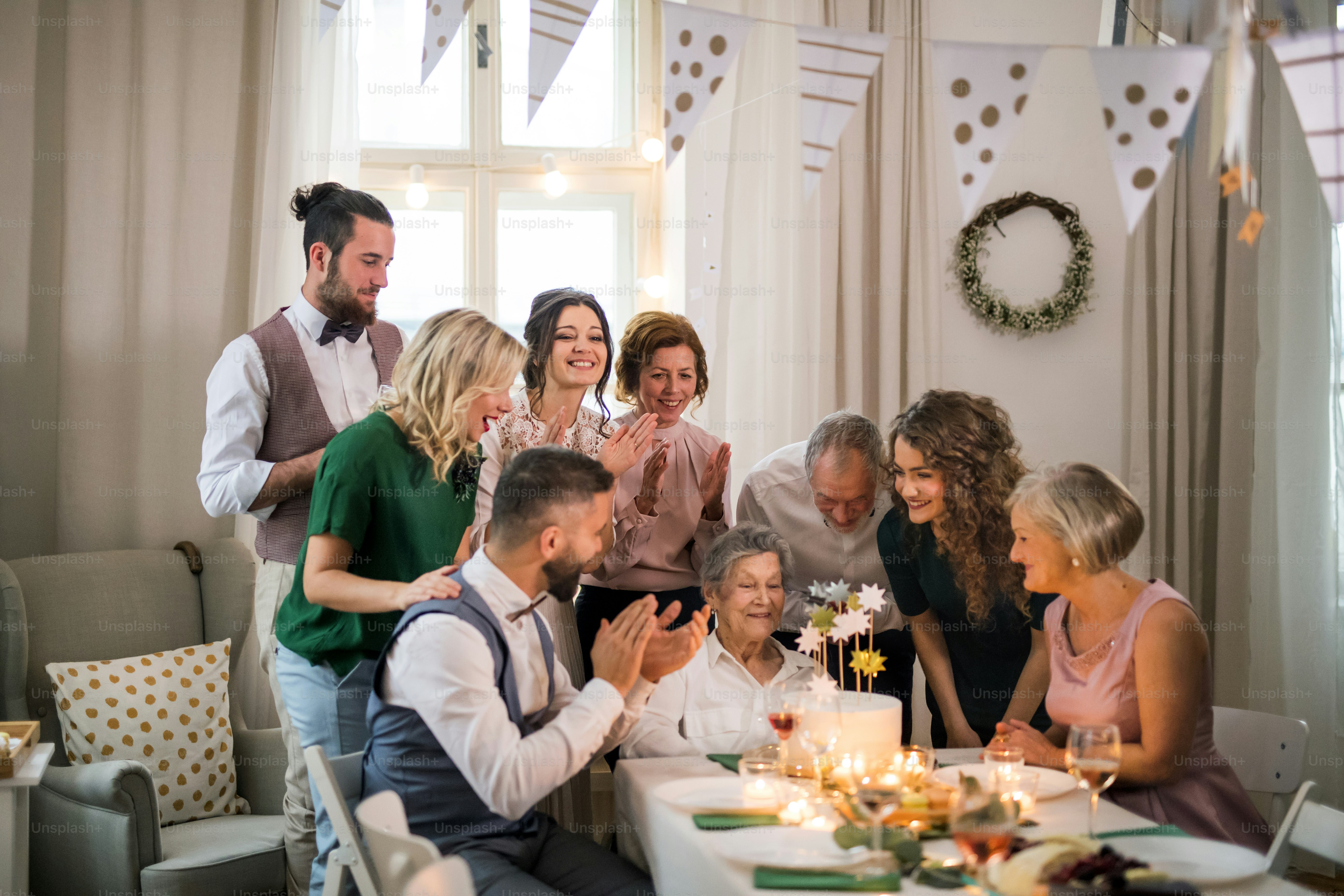 Eine ältere Frau mit Mehrgenerationenfamilie und einer Torte feiert Geburtstag auf einer Indoor-Party.