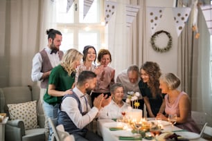 Une femme âgée avec une famille multigénérationnelle et un gâteau célébrant son anniversaire lors d’une fête à l’intérieur.