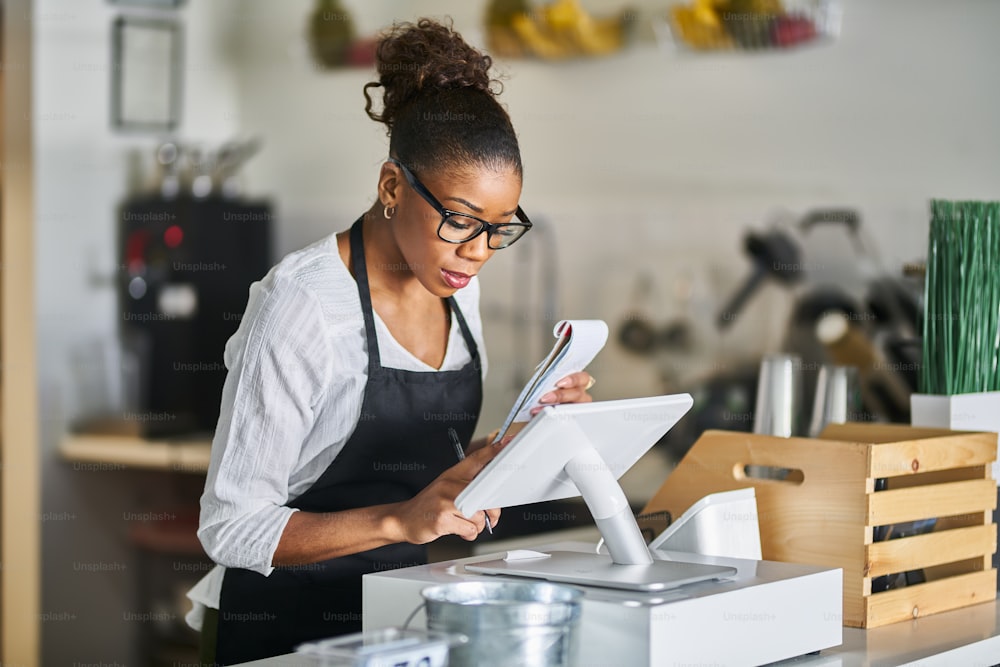 shop assistant placing order from notepad into pos point of sale terminal at register in restaurant during the day