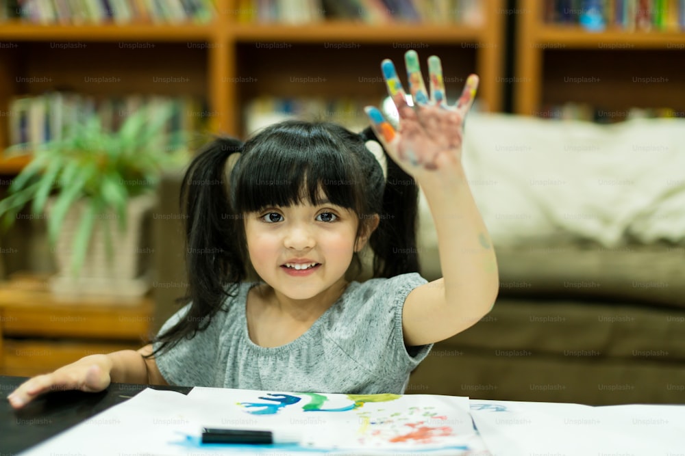La niña alegre disfruta de la pintura de colores con ideas de creatividad presentes y mano desordenada en casa