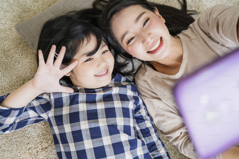 happy Asian Family mother  and daughter making a selfie photo while use  in living room home background.