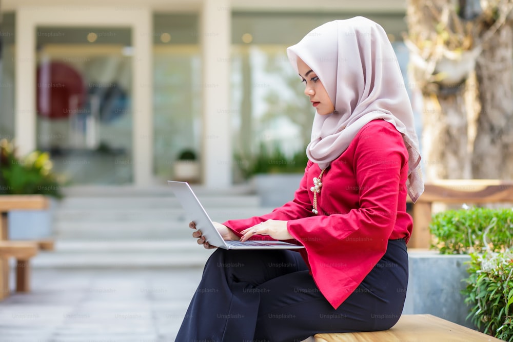 Young asian muslim woman working on laptop outdoor.
