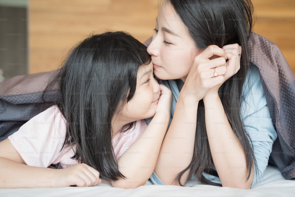 mother kisses her Daughter cheek. and hugging in the bedroom .Happy Asian family