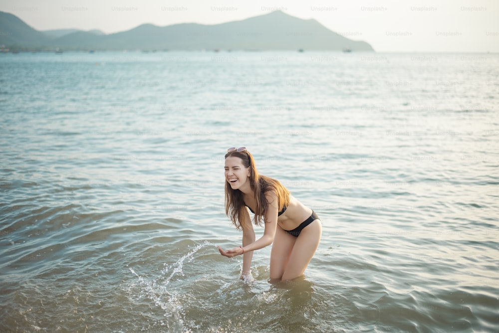 Schöne Frau im schwarzen Bikini genießt mit Meerwasser am Strand
