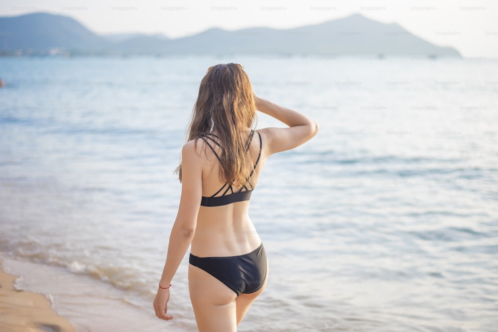 Schöne Frau im schwarzen Bikini entspannt am Strand, Sommerkonzept