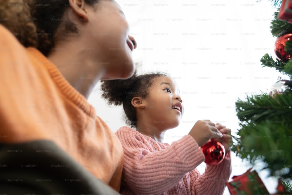 Mother and daughter african american girl decorating Christmas tree with ,arranging the christmas lights and having fun