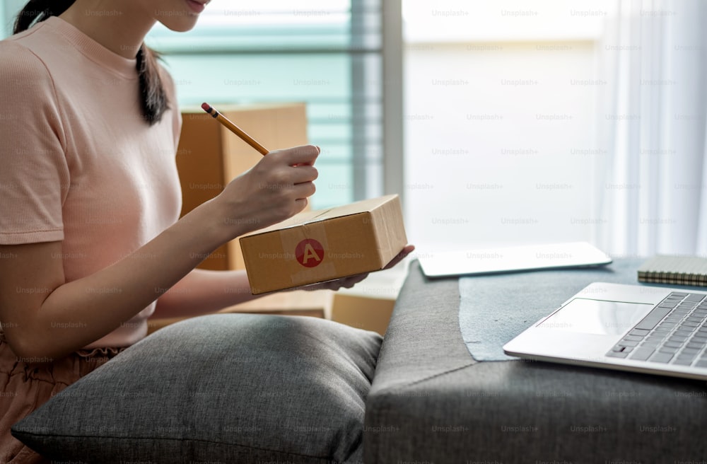 Asian woman student and small businesses online working at home taking note the customer order.