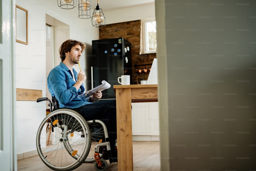 Pensive businessman in wheelchair analyzing paperwork while working at home. Copy space.