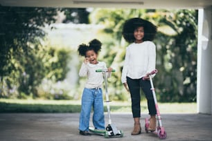 Two girls sisters are enjoying playing a scooter.