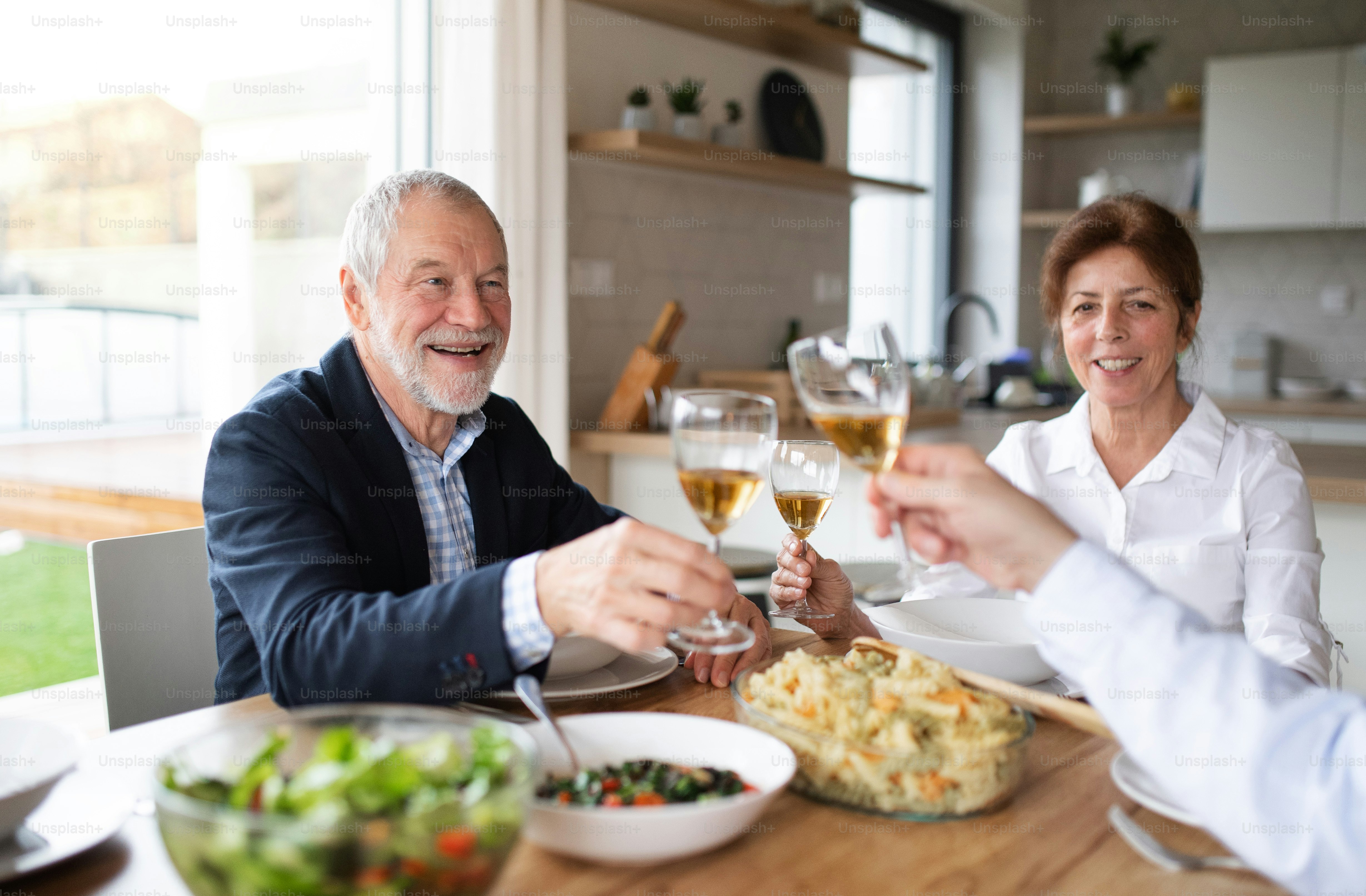 Gruppo di amici anziani che si godono la cena a casa, facendo tintinnare i bicchieri.