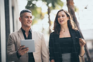 Happy businessman showing content on tablet to female colleague. Business man and woman walking outside