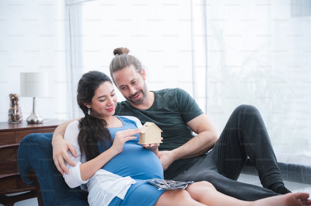 Die Familie der schönen schwangeren Frau und ihr gutaussehender Ehemann lächeln, während sie Zeit miteinander im Bett verbringen. Mann berührt und hört Baby im Bauch Glückliches Konzept