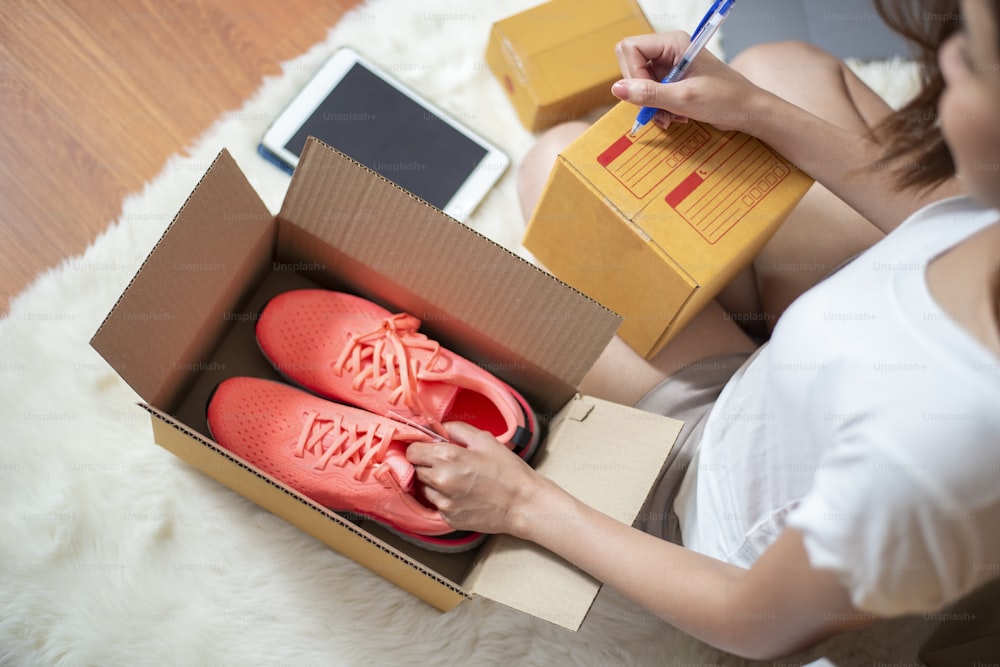 Woman entrepreneur owner SME business is checking order with smartphone, laptop and packaging box to send her customer