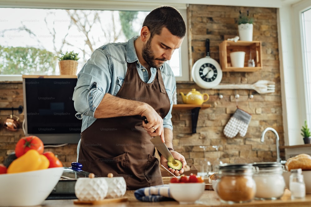 Young man preparing healthy food and peeling avocado in the kitchen.