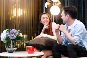 happiness young asian couple marry family enjoy tv show and good conversation embrace together hand hold coffee drink laugh smile together on sofa couch in living room home interior background