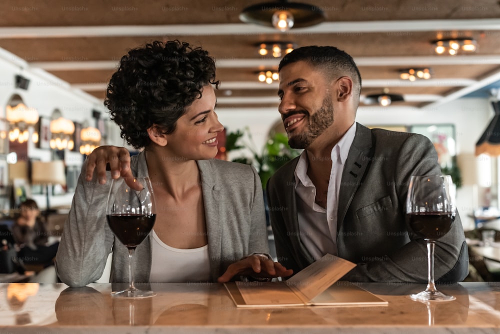 Young lovely couple enjoying at the bar in the evening. They are sitting at the bar with a glass of wine.