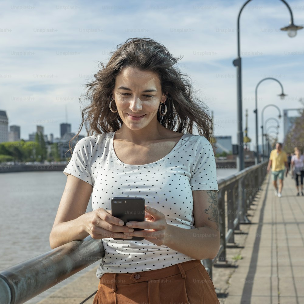 Una joven sonriente enviando mensajes de texto por teléfono en Puerto Madero, Buenos Aires