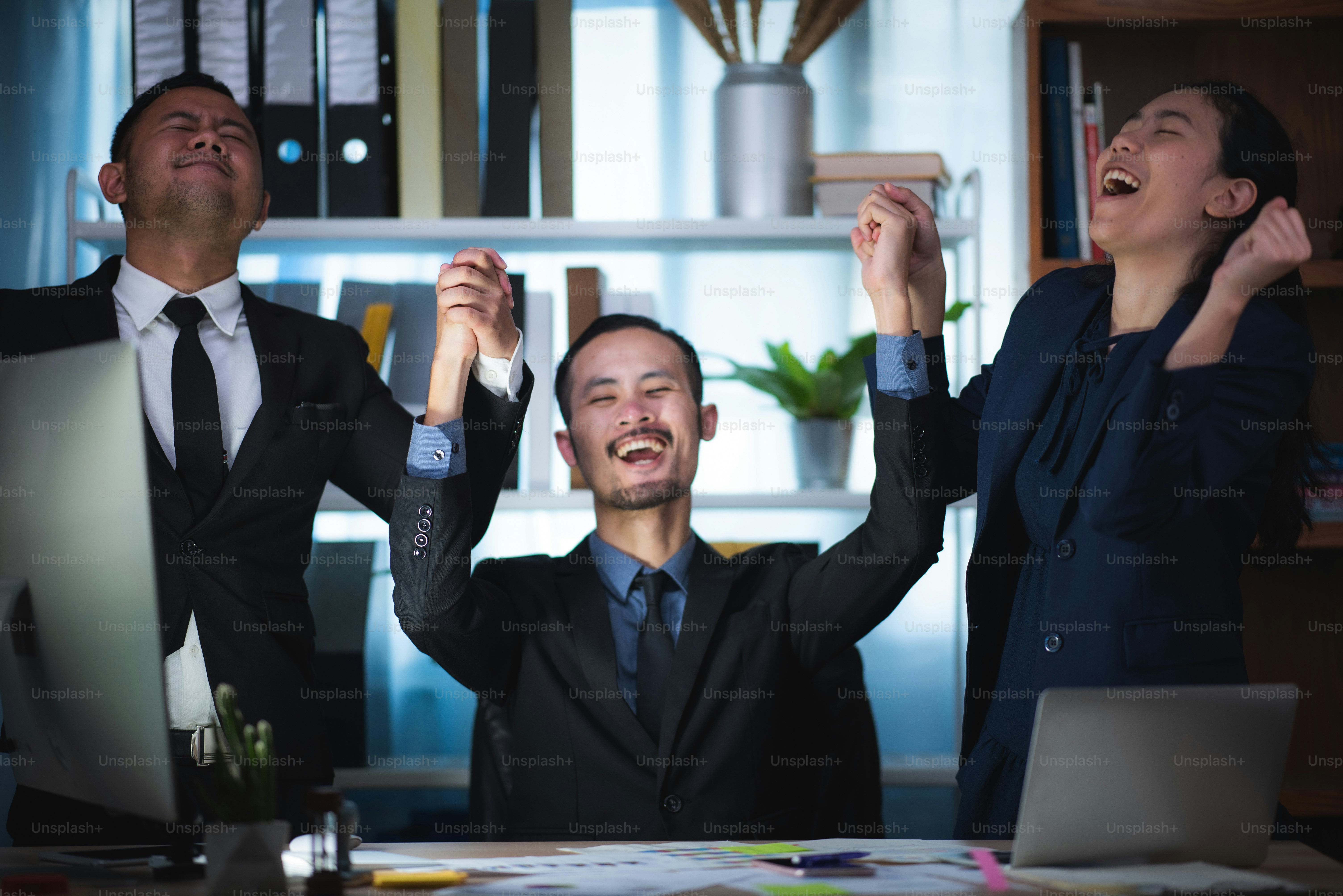 Three excited employees reading good news online in a computer sitting in a desktop at office